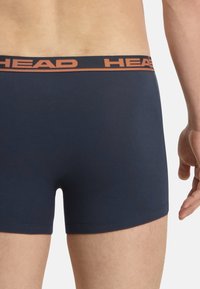 Boxer-briefs bleu marine avec une taille élastique arborant "HEAD" en orange. Texture lisse et design ajusté, montrant la vue de dos.