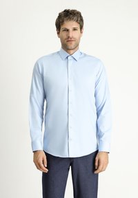 Jasnoniebieska koszula z długim rękawem, z usztywnianym kołnierzykiem i zapinana na guziki z przodu, wykonana z gładkiej tkaniny, zestawiona z ciemnymi spodniami.