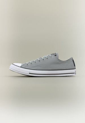 Pantof sport gri din pânză, cu talpă albă din cauciuc, vârf întărit și detaliu cu dungi negre, prezentat în profil lateral pe un fundal neutru.