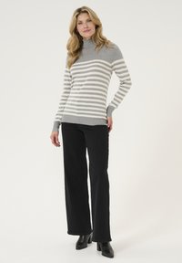 Maglione a collo alto grigio a righe con strisce orizzontali bianche, texture morbida, abbinato a pantaloni neri a gamba larga e stivali neri con tacco.