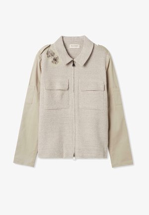 Lysebeige jakke med strikket front, lynlås, to klaplommer, glatte ærmer i stof og dekorerede broderede sommerfugle på skulderen.