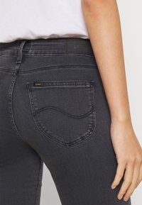 Jeans de mezclilla negra con un bolsillo trasero curvado con acento de logo dorado, detalles cosidos y diseño de ajuste slim.