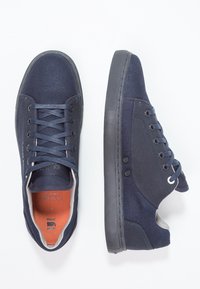 Mörkblå canvas-sneakers med rund tå, flat gummisula och snörning. Har öljetter och kontrasterande insida.