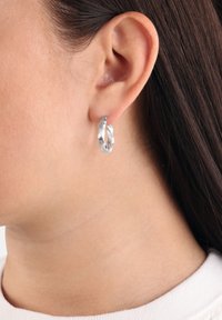 Tvistad silverörhäng som visas på ett öra, med en polerad yta och slät textur. Nära bild framhäver designdetaljer.