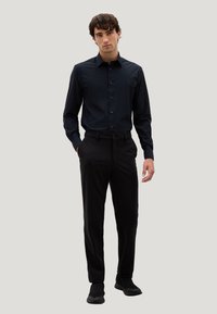 Camicia nera a maniche lunghe con colletto, abbinata a pantaloni neri e scarpe antiscivolo. Tessuto morbido e taglio su misura.