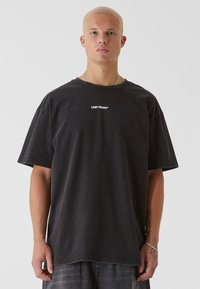 Černé bavlněné oversized tričko s žebrovaným kulatým výstřihem a potiskem "LOST YOUTH" bílou barvou na hrudi. Krátké rukávy, volný střih.