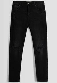 Jeans ajustados negros con rasgaduras desgastadas en ambas rodillas y un ligero desvanecimiento alrededor de los muslos, con bolsillos delanteros y traseros y cierre de botón.