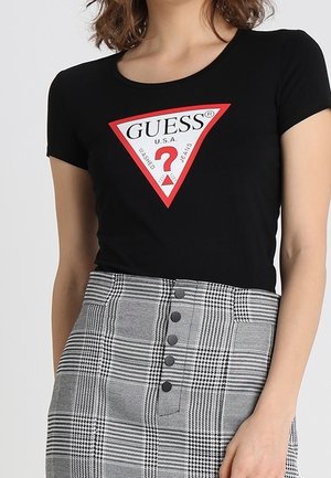 Zwart T-shirt met korte mouwen met een rood-wit driehoekig logo. Gecombineerd met een grijze geruite rok met zwarte knopen.