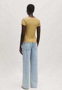 Fitted khaki T-shirt met korte mouwen, gecombineerd met lichtblauwe wijde jeans met achterzakken. Soepele texturen en een eenvoudig ontwerp.