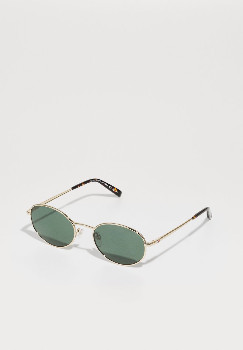 Green-tinted sunglasses with an oval lens shape, thin gold metal frame, and black textured temple accents featuring brand logo.