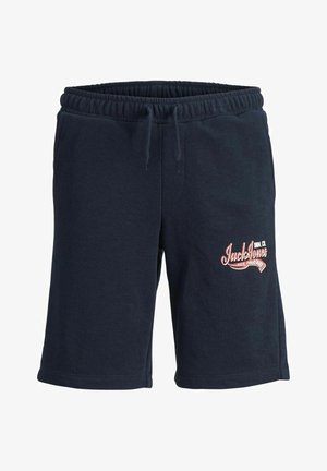 Szary sweatshirt z logo z przodu, w połączeniu z granatowymi szortami z czerwonym logo. Białe trampki i widoczne białe skarpetki dopełniają stylizację.