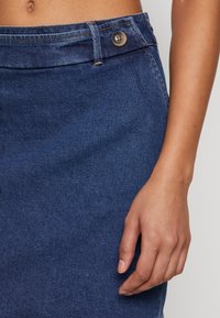 Jeanskjol i mörkblått med knappstängning, med en slät yta och klassisk design. Inkluderar en framficka och diskret sömnad.