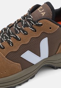 Brown suede and mesh sneaker with a white logo, black and white laces, textured upper, and a durable rubber sole for traction.