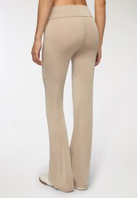 Pantaloni beige a palazzo realizzati in un tessuto morbido e elasticizzato, con un ampio girovita. Presentano una finitura pulita senza cuciture o motivi visibili.