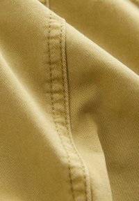 Tessuto di cotone in una morbida tonalità di giallo, che mostra una texture a coste diagonali con cuciture visibili e leggere corrugazioni lungo le cuciture.