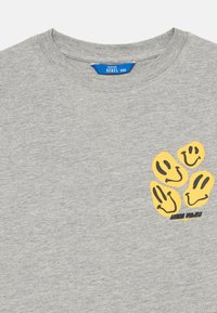 Lys grå crew neck t-shirt med fire gule smilende ansigt grafik og "good vibes" tekst på den øverste venstre brystområde.