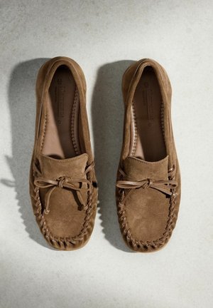 Para brązowych mokasynów zamszowych z przeszyciami i kokardkami, widziana z góry na jasnej powierzchni.