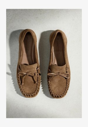 Barna színű szarvasbőr mokaszin félcipő pár, varrott részletekkel és masnival, felülnézetből világos felületen.