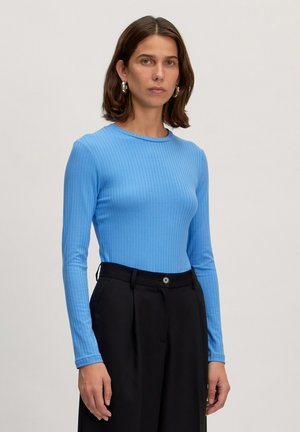 Blauwe geribbelde langemouwen top met een ronde hals, gedragen met zwarte hoog-waisted broek. De stof lijkt zacht en licht rekbaar.