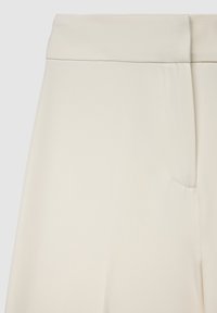 Pantalon sur mesure couleur crème avec une texture lisse, doté d'une ceinture plate et d'une unique poche latérale. Design simple sans motifs.