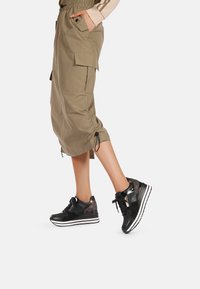 Sneaker sportive nere con pannelli testurizzati, strisce bianche sulla suola e dettagli a contrasto. Indossati con pantaloni cargo larghi color khaki.