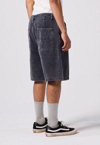 Shorts en velours côtelé gris foncé avec une surface texturée, dotés d'une poche arrière et d'un design droit. Portés avec des chaussettes grises et des baskets noires.