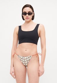 Haut de bikini noir court avec décolleté carré, associé à un bas crème à motifs avec des liens orange et des designs floraux.