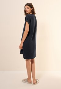Navyblaues, leichtes Kleid mit kurzen Ärmeln, lässiger Passform und strukturiertem Stoff; Modell trägt hellfarbige Slippers.