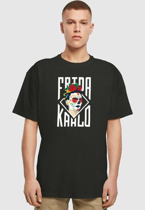 Svart bomull T-skjorte med et Frida Kahlo-trykk som har en blomsterkrans, dristig rød og hvit fargepalett, og en diamantformet bakgrunn.