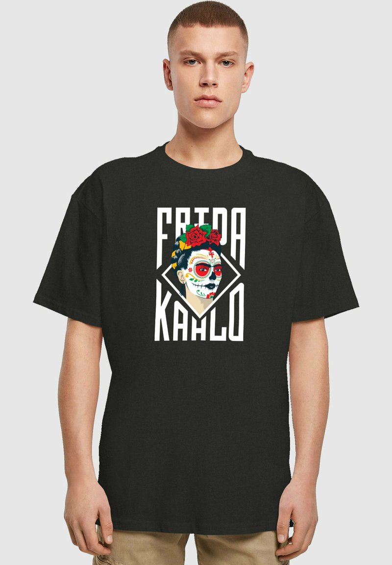 Svart bomull T-skjorte med et Frida Kahlo-trykk som har en blomsterkrans, dristig rød og hvit fargepalett, og en diamantformet bakgrunn.