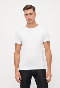 White crew-neck t-shirt in a slim fit, short sleeves, lightweight fabric, smooth texture, paired with black fitted pants. Minimalist design.