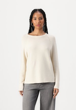 Light cream knit sweater with a wide neckline and long sleeves, featuring a ribbed texture. Paired with gray, loose-fitting jeans.