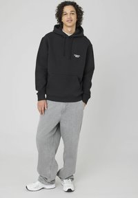 Sweat à capuche noir avec une poche avant, mettant en avant un texte blanc. Assorti à un jean baggy gris clair et des chaussures de sport blanches.