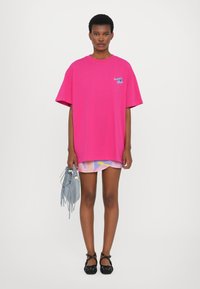 Svetlo roza prevelik t-shirt z grafiko "lepota", kratkimi rokavi, kombiniran z vzorčasto pastelno krilo in sivo torbico s resicami. Črne balerinke.