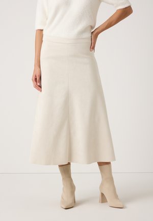 Een crèmekleurige A-lijn rok van zachte stof met een gladde textuur, voorzien van een hoge taille en een rok die tot op de knie reikt. Gepaard met lichtbeige laarzen.