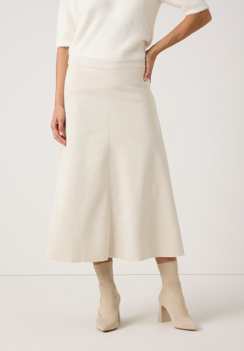 Een crèmekleurige A-lijn rok van zachte stof met een gladde textuur, voorzien van een hoge taille en een rok die tot op de knie reikt. Gepaard met lichtbeige laarzen.