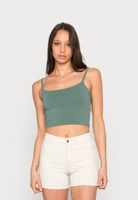 Crop top verde em algodão com alças de espaguete ajustáveis e um design ajustado, combinado com calções de ganga brancos com bainha desfiada.