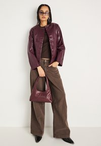 Burgundská kožená bunda so zapínaním na patentky, hnedý priliehavý top, široké hnedé nohavice a zodpovedajúca taška. Čierne topánky s ostrou špicou.