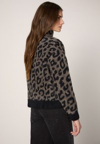 Sweter w panterkę w odcieniach beżu i czerni; miękka, teksturowana tkanina z krótkim krojem i jednolitym czarnym mankietem.