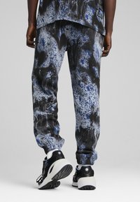 Mønstret joggebukser i flere farver med et blåt og sort abstrakt mønster, lavet af blødt stof med en afslappet pasform, parret med sorte sneakers.