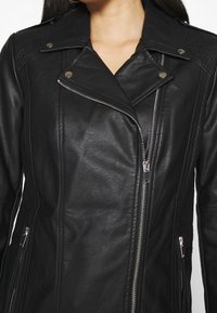 Giacca biker in pelle nera con zip diagonale, colletto a scatto e accenti trapuntati sulle spalle. Presenta cerniere di colore argento su tasche.