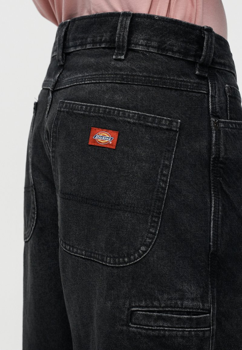 Zwarte spijkerbroek met een klassiek ontwerp en achterzakken. Op de rechter achterzak is een rood-blauw Dickies-logo zichtbaar.
