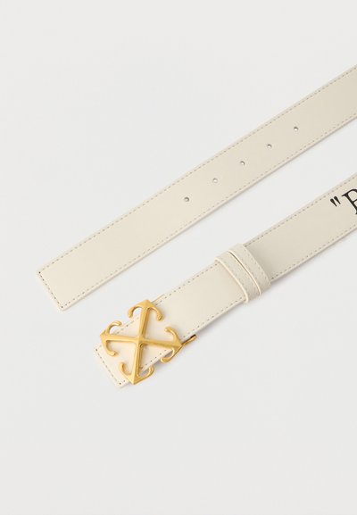 Δερμάτινη ζώνη σε κρεμ χρώμα με χρυσή διακοσμητική αγκράφα σε σχήμα σταυρού και πέντε τρύπες ρύθμισης σε λευκό φόντο.