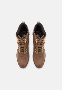 Stivali da trekking in suede marrone con hardware dorato, fodera nera a contrasto, lacci e doppie cerniere laterali per un facile accesso.