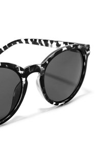 Černobílé sluneční brýle s kulatými skly, silným rámečkem a výrazným kočičím tvarem. Hladký povrch s jemným lesklým finišem.