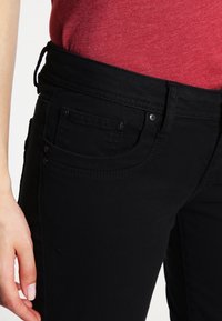 Jeans en denim noir au design ajusté. Comprend des poches avant, une ceinture robuste et un tissu texturé.