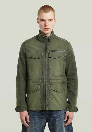 Veste vert olive en tissu résistant, avec un col montant, une fermeture éclair sur le devant, quatre poches à rabat et des coutures double couture.