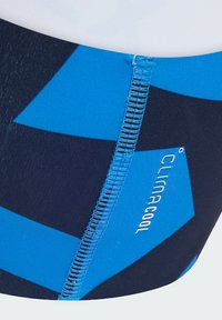 La ropa de baño ClimaCool presenta patrones geométricos azules sobre un fondo oscuro, con costuras de contraste visibles y detalles del logo.