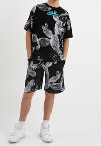 Conjunto de camiseta de manga corta negra y pantalones cortos con un estampado de cactus blanco. La camiseta tiene una etiqueta turquesa que dice "WHITE OR BLACK." Zapatillas blancas.