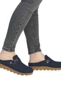 Mørkeblå filtsavedækker med en struktureret korksål, der har en sidespænde og afrundede kanter. Båret med tætsiddende grå jeans.